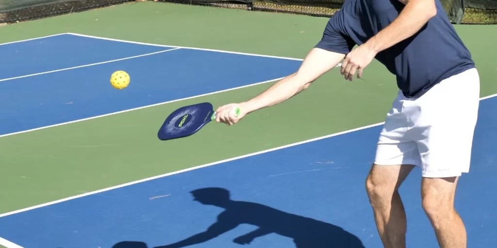 a player is playing pickleball along with paddle in his hand and pickleball in air