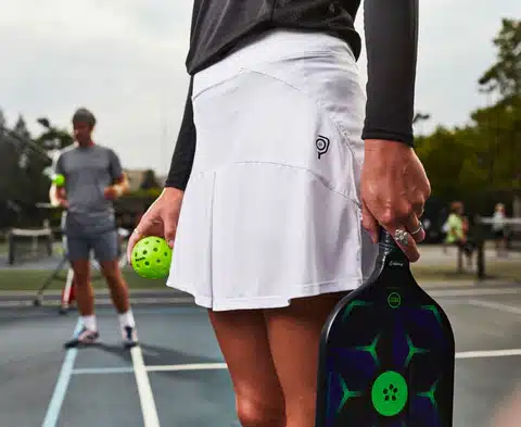 a women standing in the game court while having a pickleball and paddle in her hands