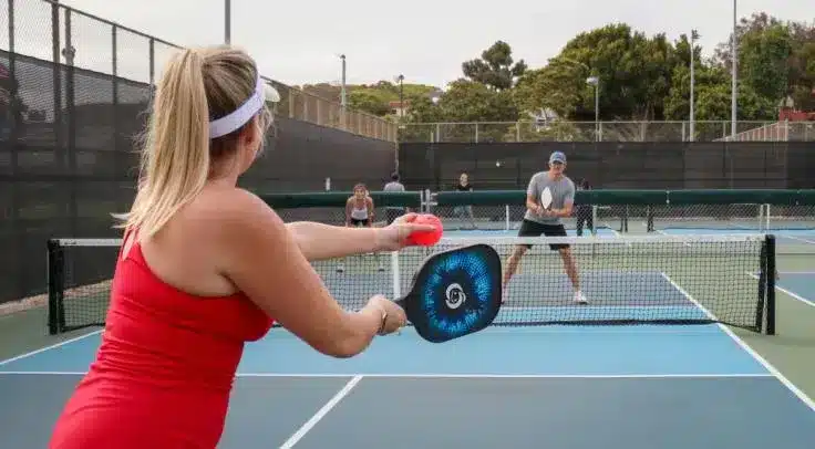 A backview of lady in red playing pickleball against her opponent