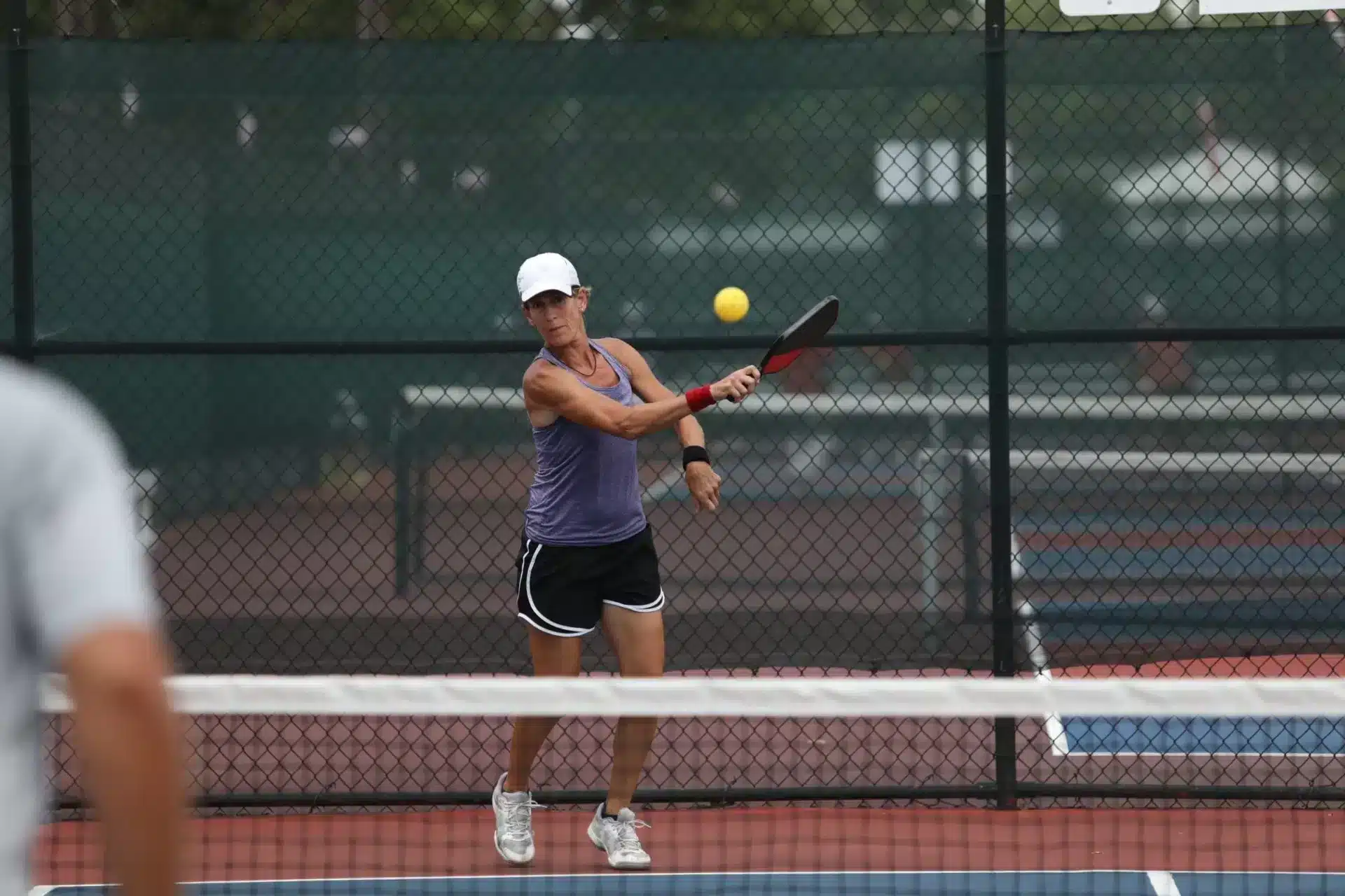 A view of a lady serving in pickeball next to a net