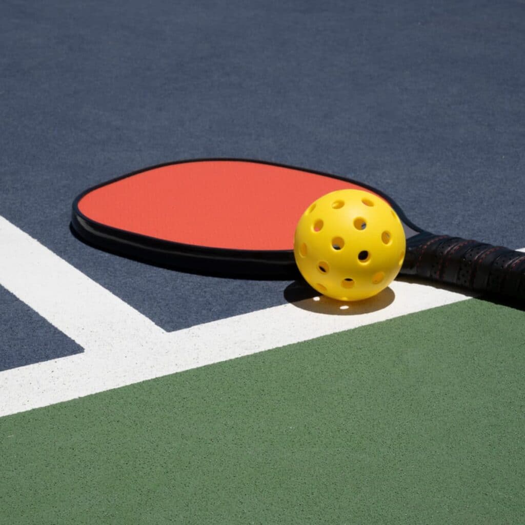 A view of a paddle with a pickleball on a court surface