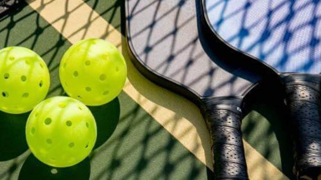 A view of three pickleballs with two paddles