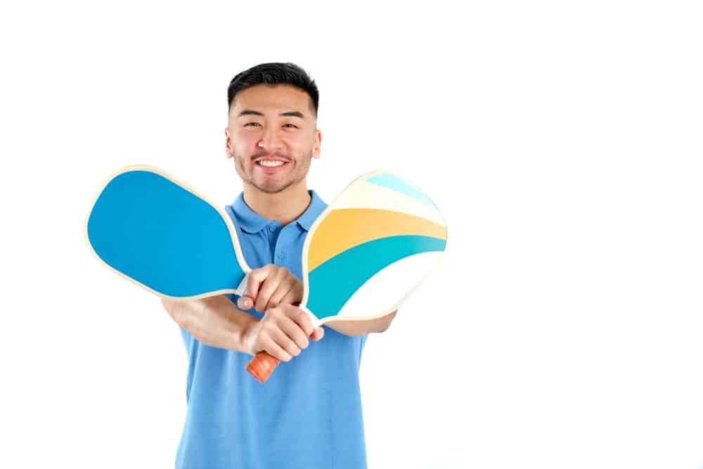 A front view of a guy holding two pickleball paddles 