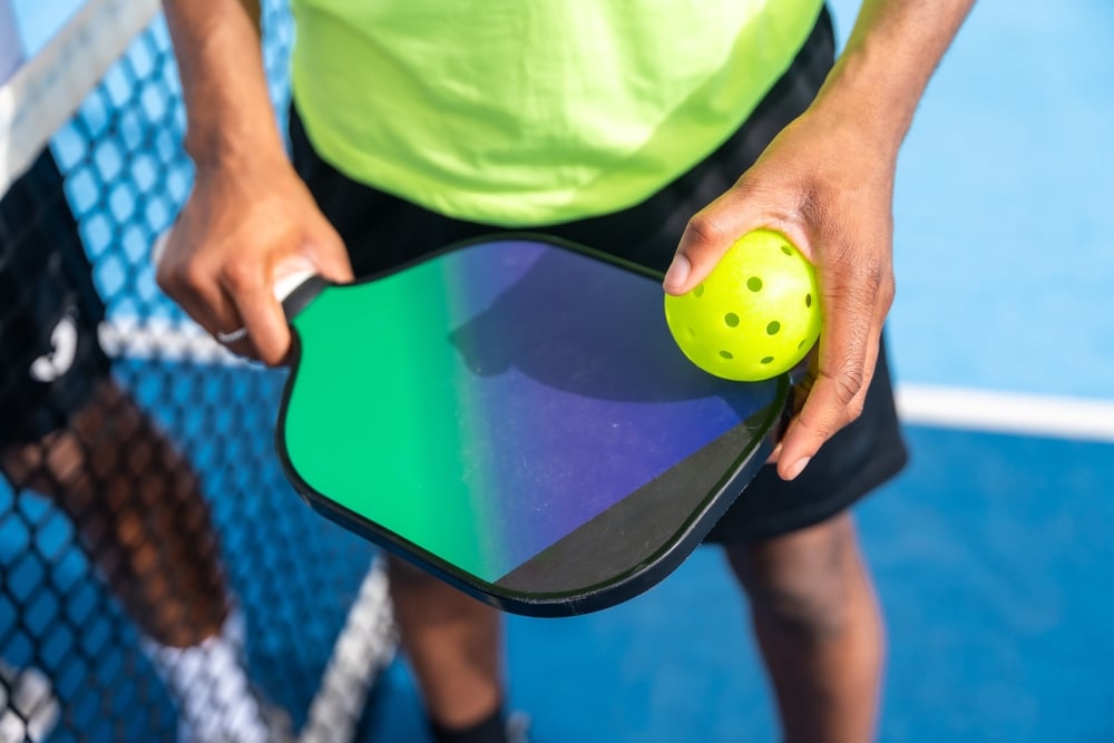 A view of a person holding a pickleball paddle and a ball