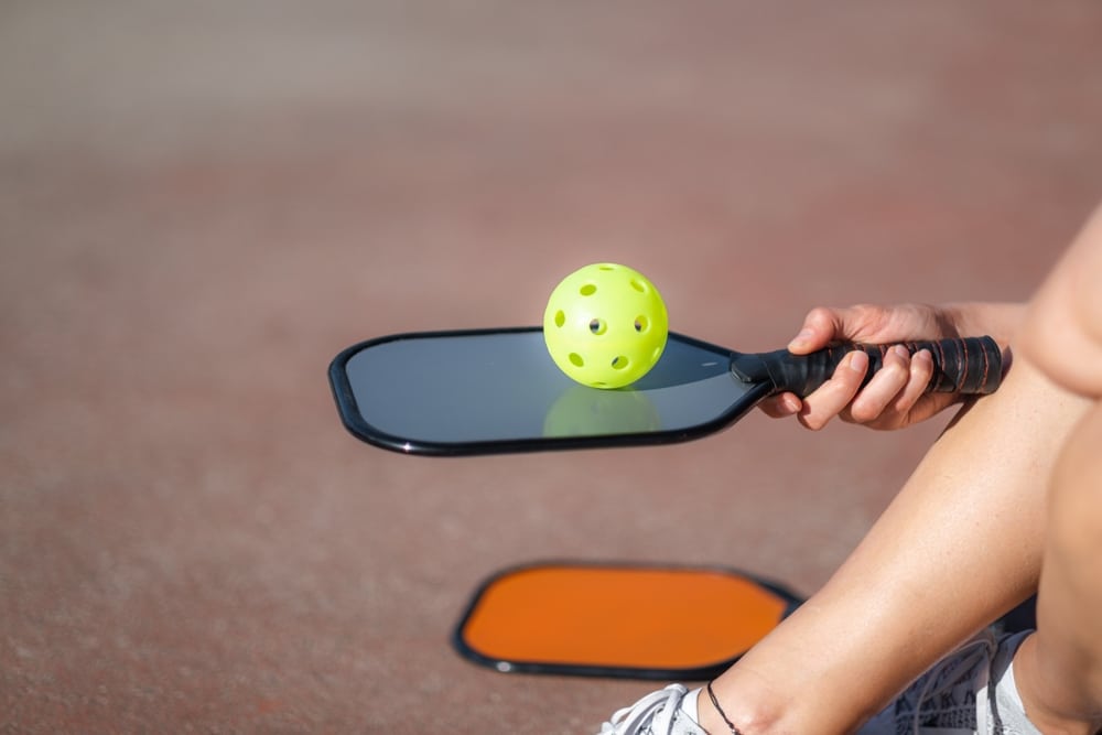 A view of a person holding a pickleball paddle with a ball on it