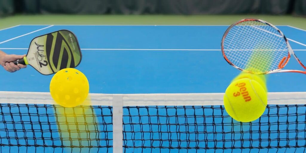 A view of a pickleball paddle on one side hitting a ball and tennis racket hitting a ball at another side