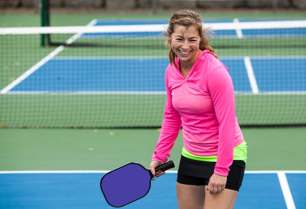 A view of a woman holding a pickleball at a court