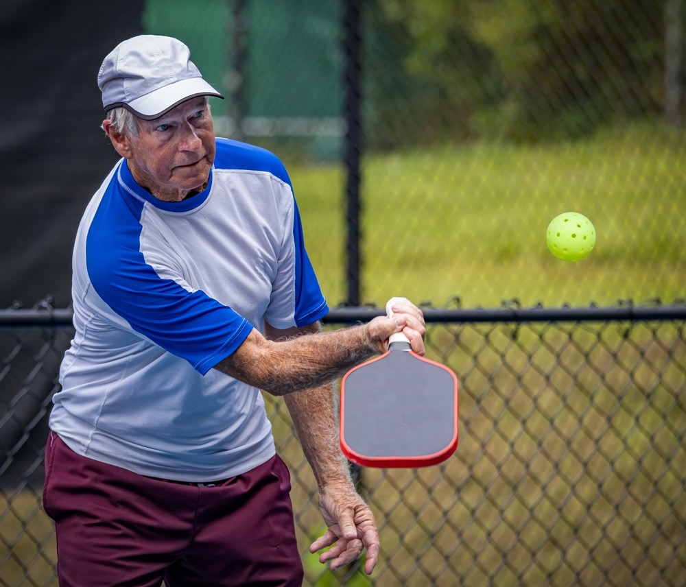 A view of am elderly man hitting a spin shot with a pickleball paddle