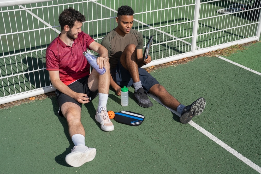 A view of two guy sitting on a pickleball ground